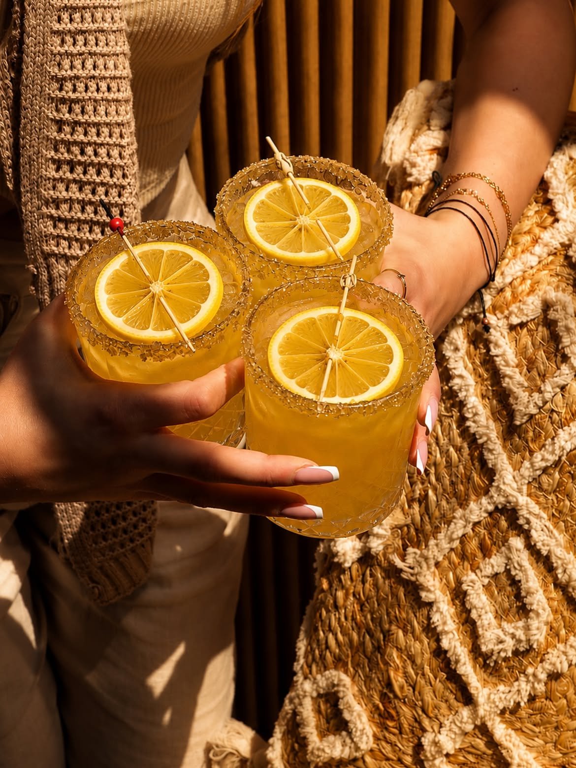 Hands holding three citrus cocktails